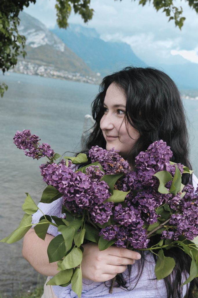 Elsa, la créatrice d'Il était une Meuf tient un bouquet de lilas avec derrière le lac d'annecy