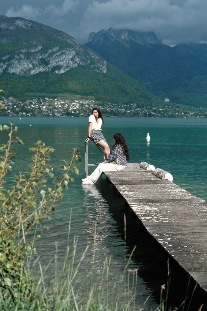 Sur un ponton du lac d'Annecy, Soraya porte un short Il était une Meuf et Elsa assise porte la veste associée